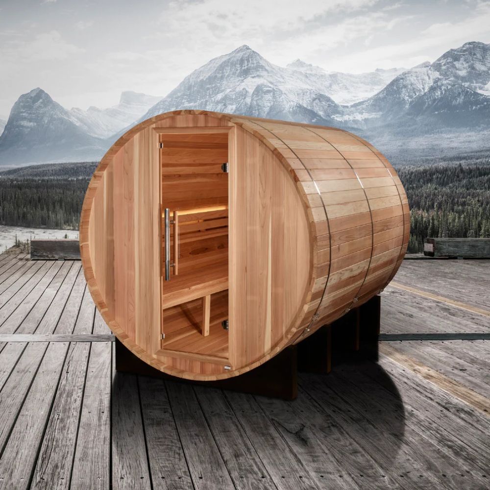 Wooden barrel-shaped sauna on a wooden deck with mountains in the background
