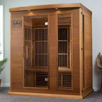 Wooden infrared sauna in a room with a plant and decorative item on the wall.